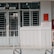 A building entrance with metal barred doors and windows, featuring signs indicating it belongs to a faculty for high-quality training. The facade is white, and there are red fire extinguishers and safety notices mounted on the wall next to the entrance.