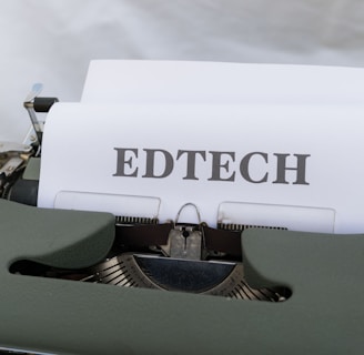 A vintage typewriter with a sheet of paper that has the word 'EDTECH' typed on it. The typewriter casing is dark green and the setting appears to be on a light wooden surface.